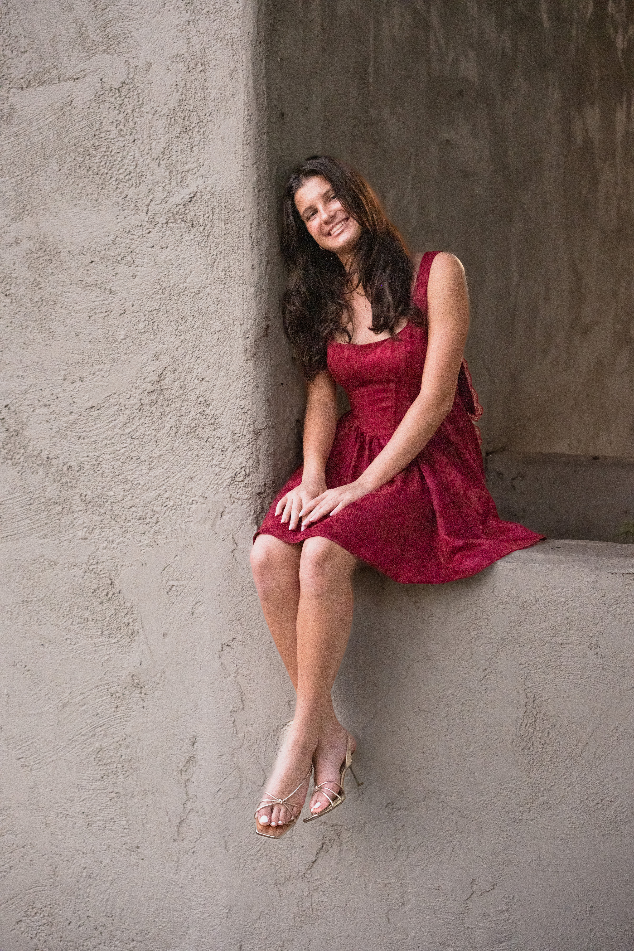 High school graduation portrait of a girl in a red dress seated during a senior photo session